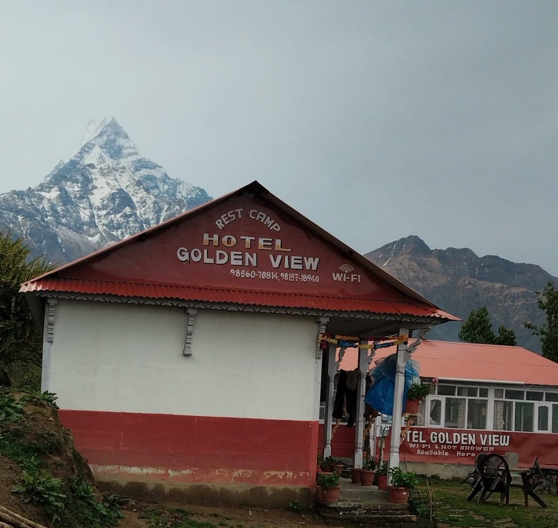 A small mountain lodge called “Hotel Golden View” stands in a rugged area, with a snowy peak rising behind it.