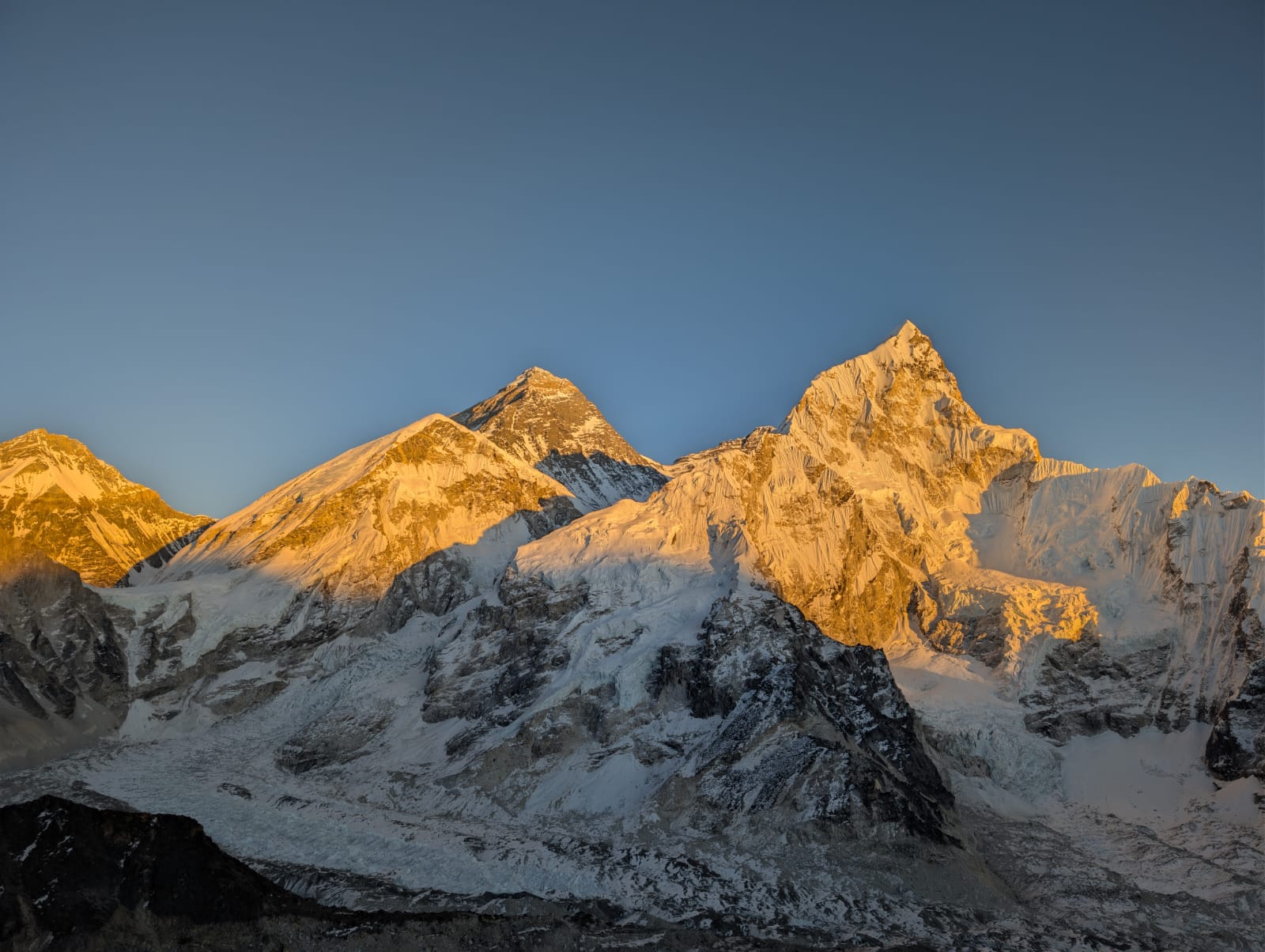 Snow-covered Himalayan mountain peaks glowing in warm sunrise light against a clear blue sky.